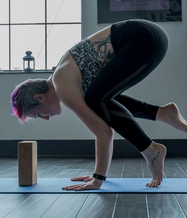 Woman performing a focused yoga balance pose in low light.